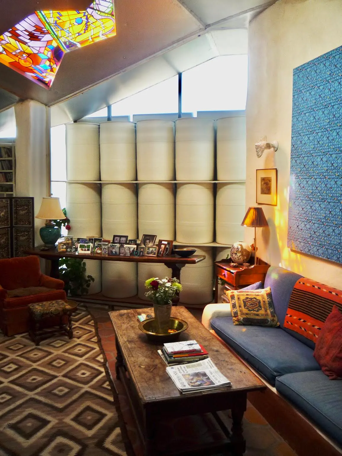 Interior of Steve Baer's zome home showing white plastic drum wall thermal mass storage, stained glass skylight, and living room